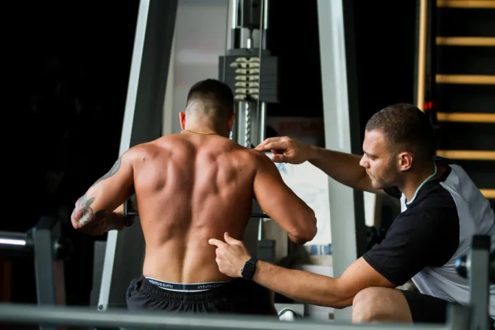 Personal trainer che corregge la postura di un ragazzo alla lat machine